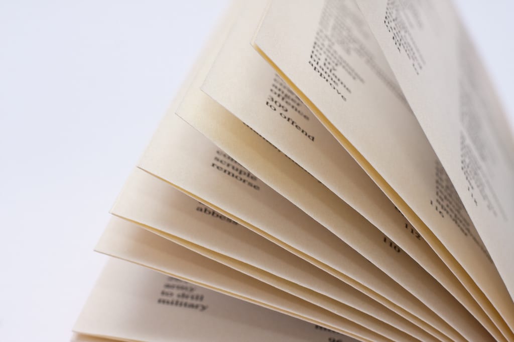 Macro of yellowed pages of a photography glossary flipping up in the air isolated against a white background.