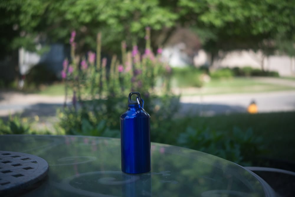 Picture of a blue metal water bottle outside on a table to show thin depth of field at wider apertures