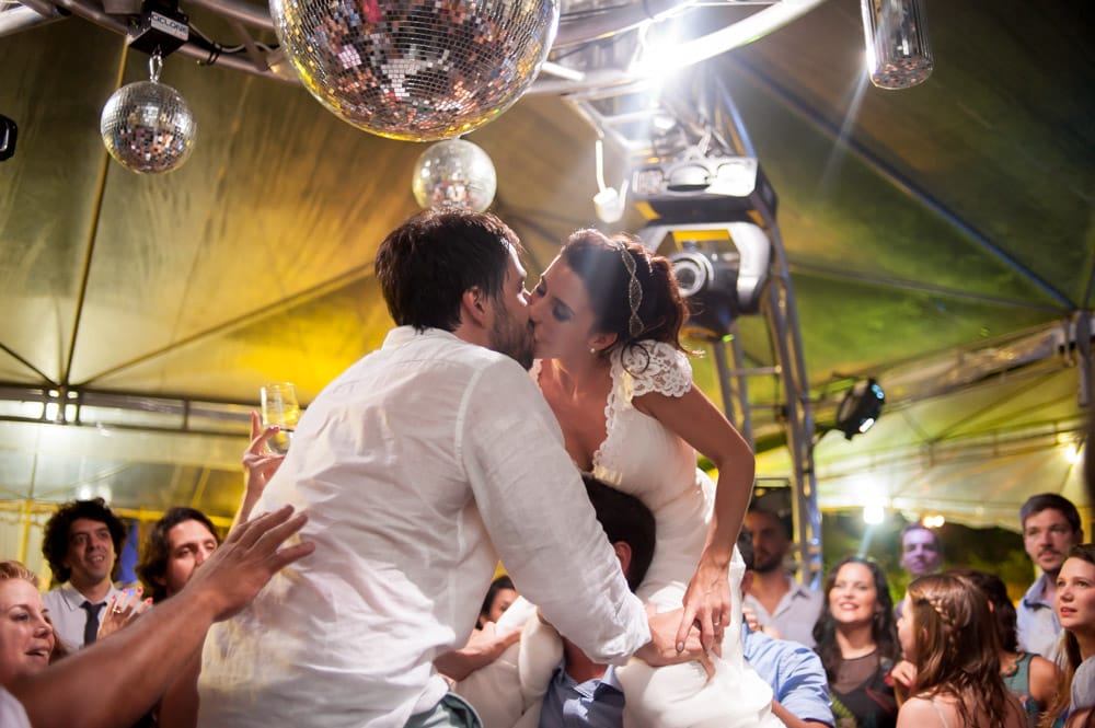 Picture of a bride and groom on the shoulders of guests on their wedding reception dance floor kissing