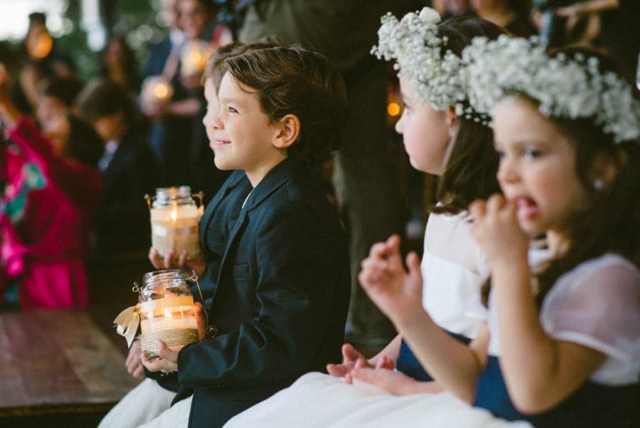 Image of kids watching wedding ceremony, one of whom is a boy holding a candle and smiling