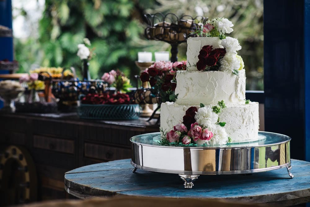 Image of a white wedding cake set up outdoors with flowers on it