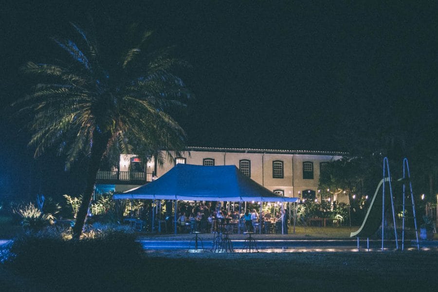 Image of a wedding venue at night with a pool, a palm tree, and a tent where people are partying under for the wedding reception