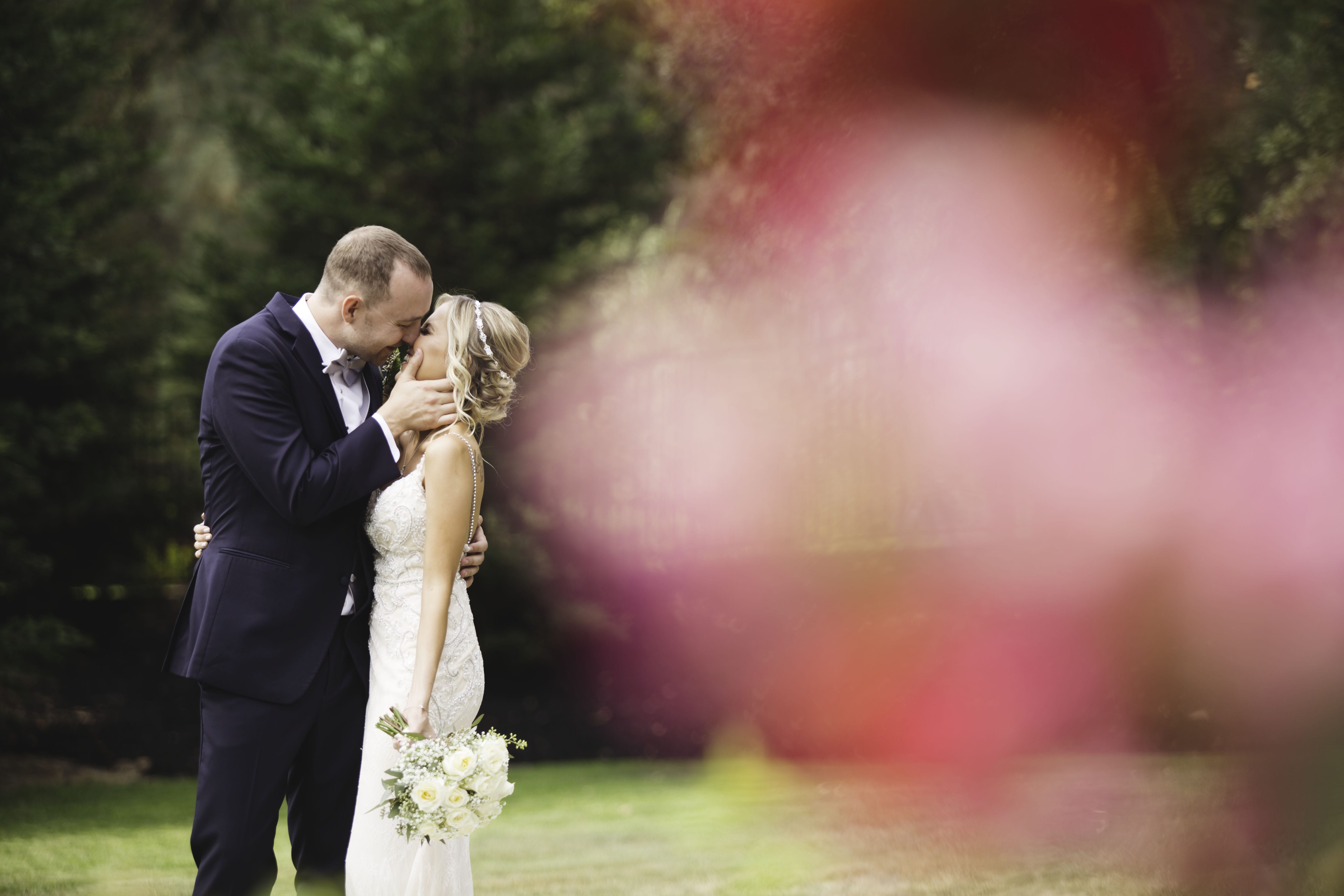 image of a bride and groom on their wedding day kissing with a red flower in the foreground