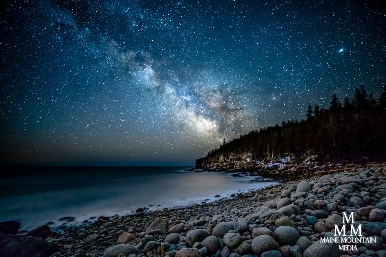 A rocky shore with a blue starry night sky.