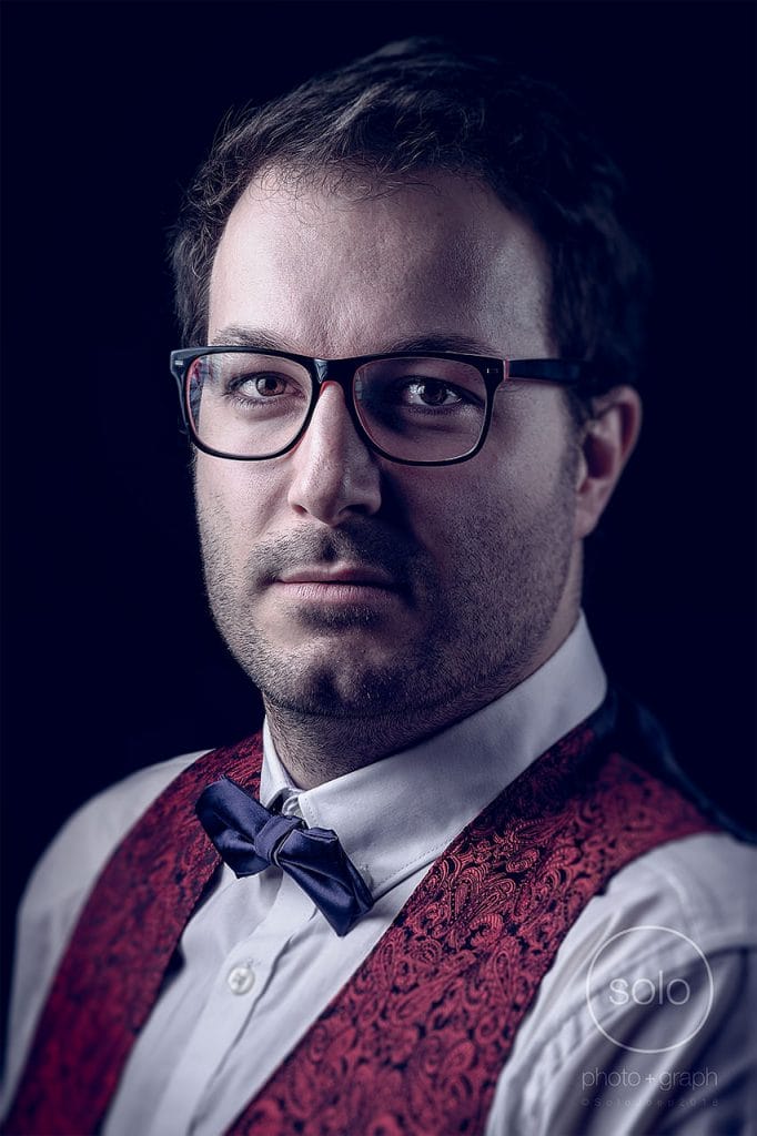 Corporate portrait of a main with glasses and a bow tie and a black background that was actually white