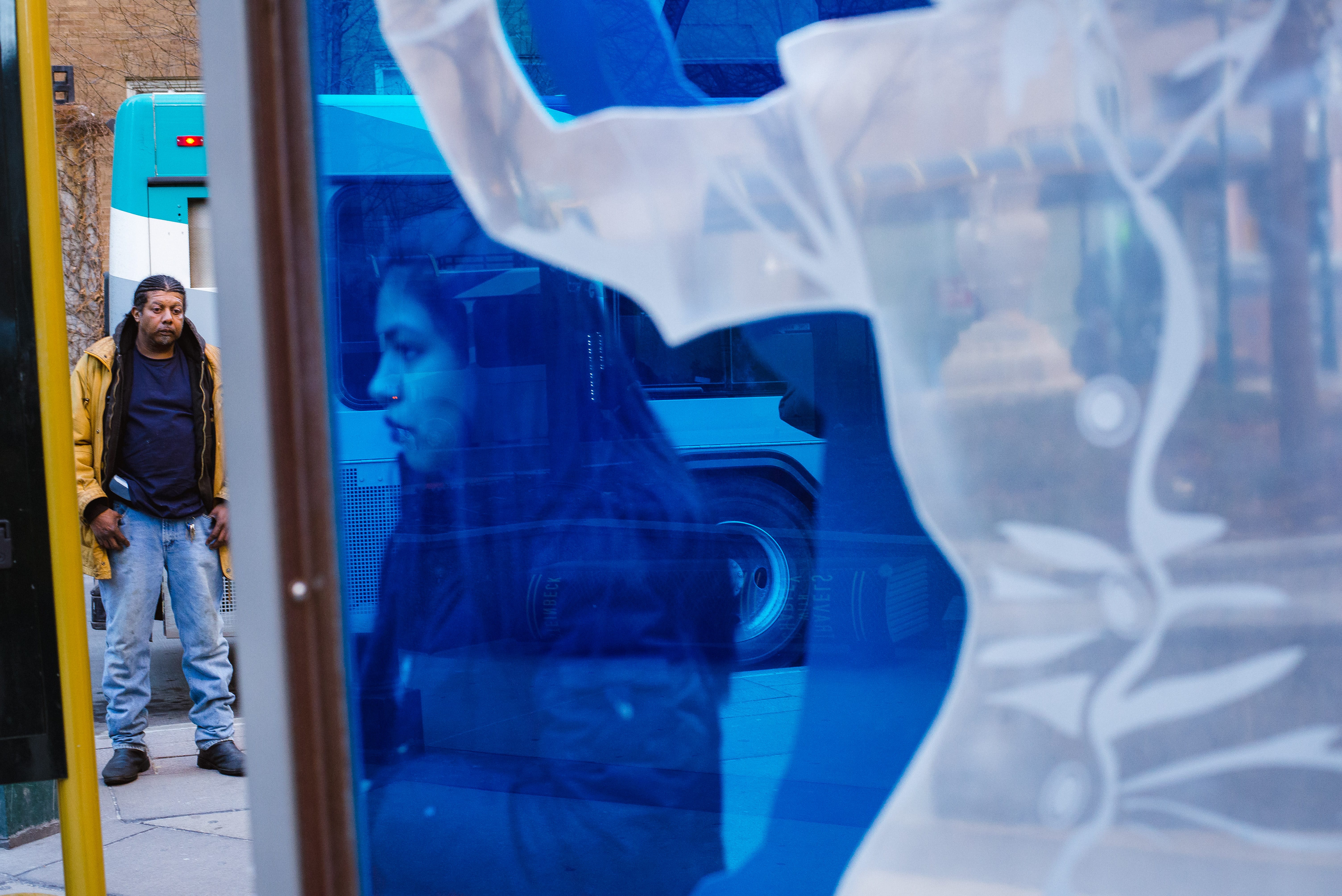 A woman behind blue glass; a man in front of a bus looking down.