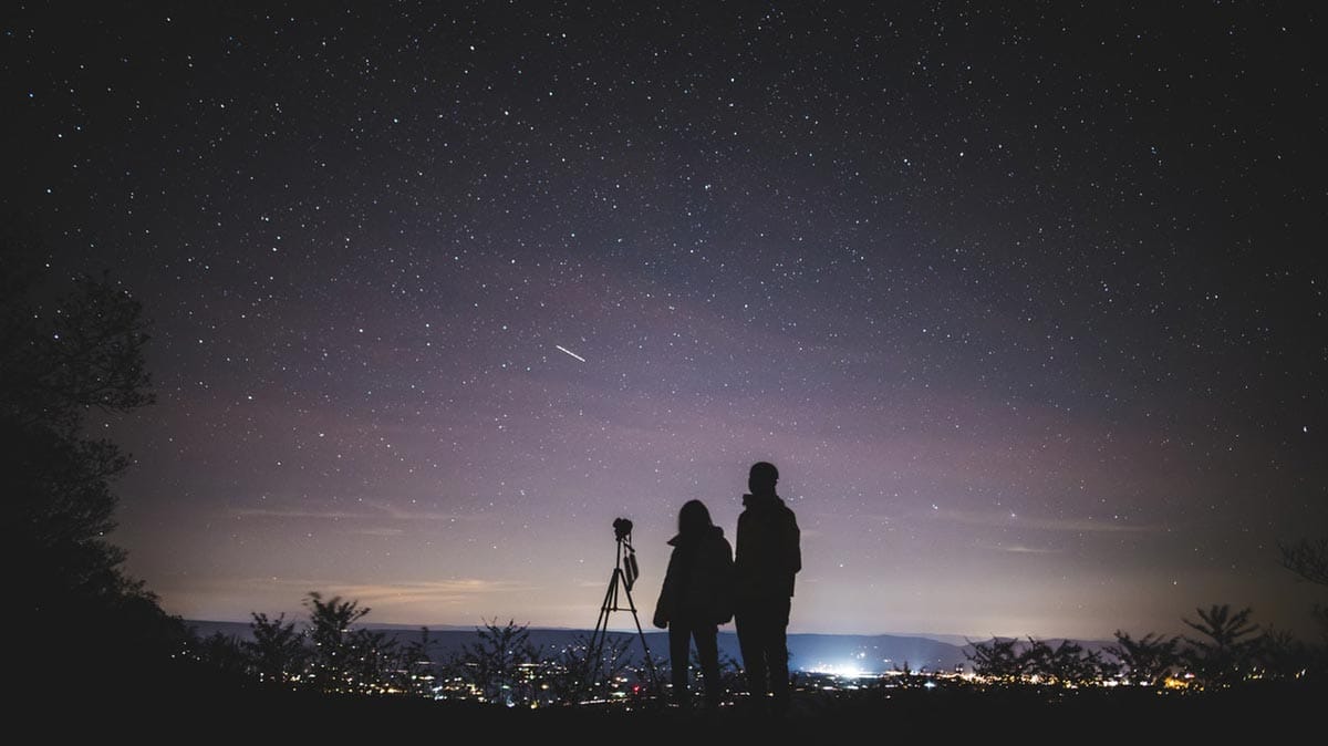 Astrophotography image of two photographers looking up at the stars with their camera on a tripod