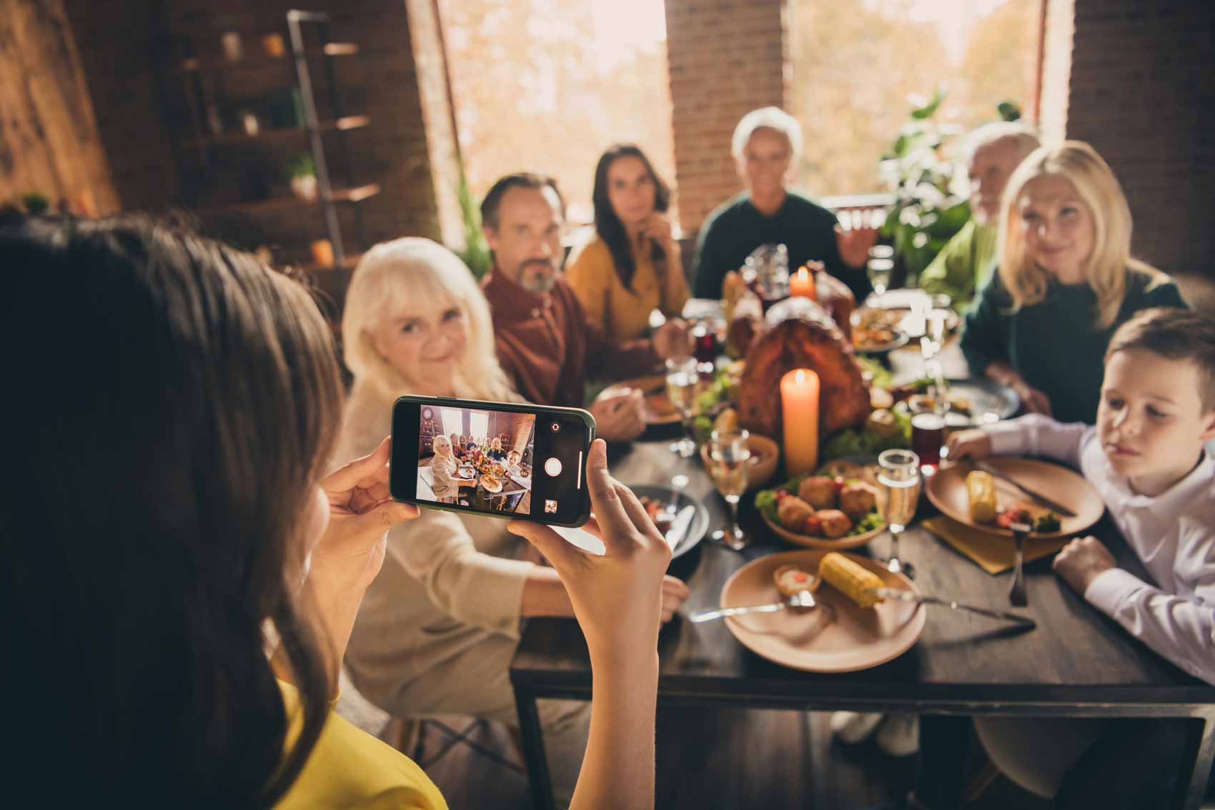 Image of a woman photographing a family at Thanksgiving dinner on her phone