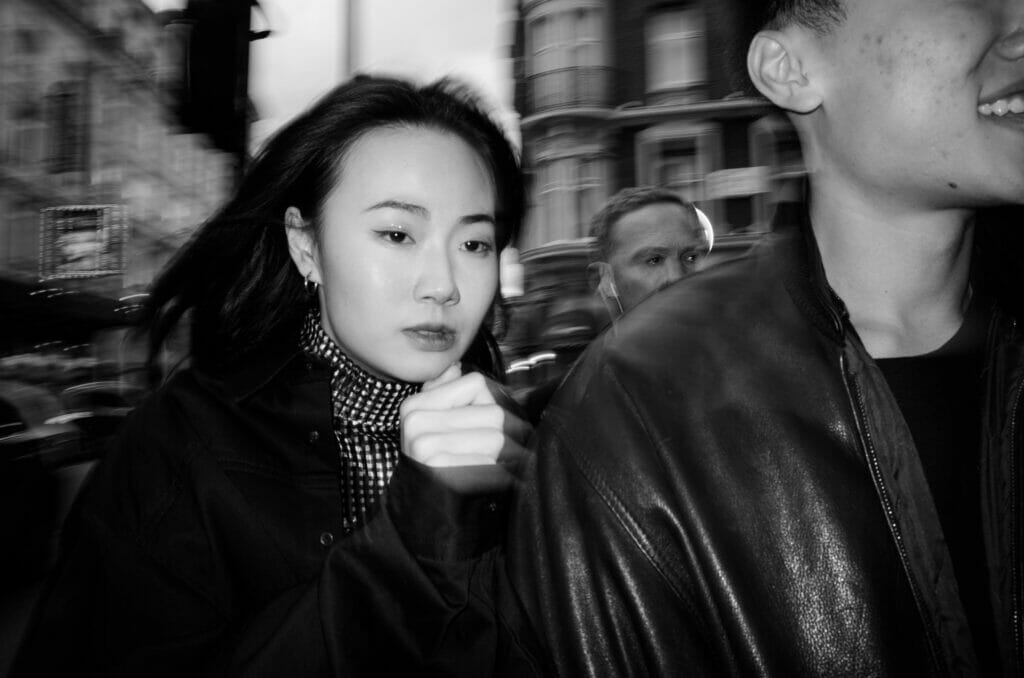A black and white photo of a woman with black hair on a public street.