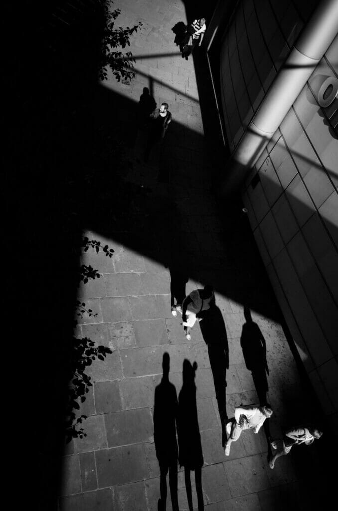 A sidewalk from above with people walking and casting long shadows.