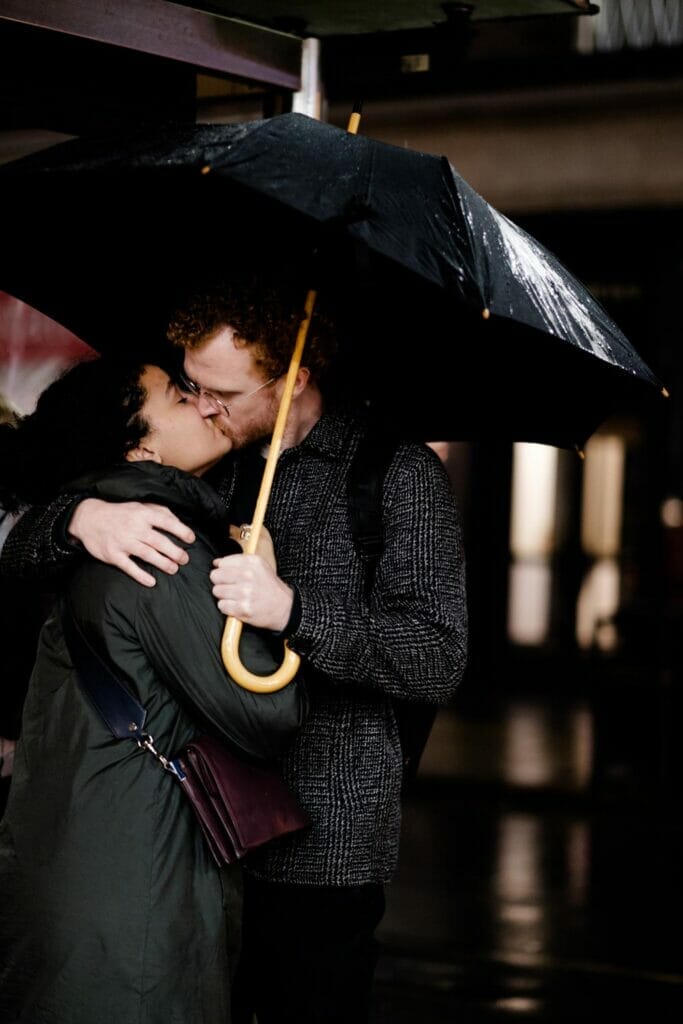 A couple kissing in the rain as the man holds an umbrella.