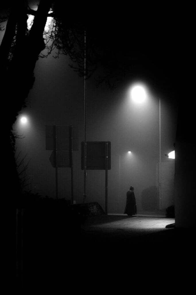 A dark night scene with a figure walking.