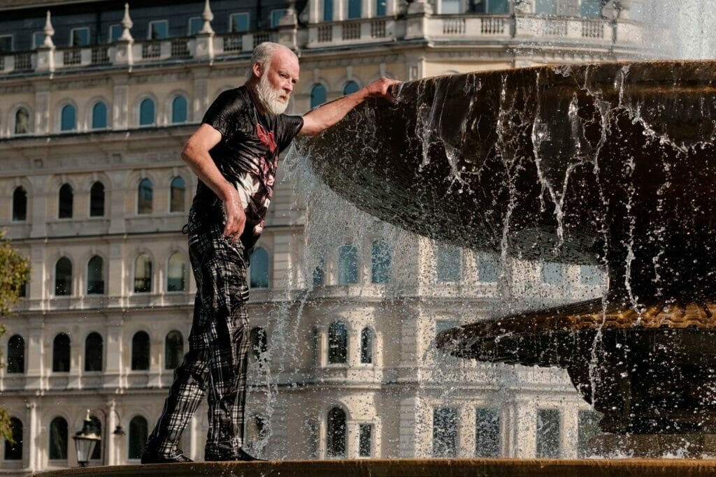 A tall bearded man soaking wet standing on a fountain.