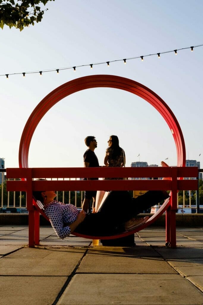 A woman laying and reading on a red circle in front of a couple.
