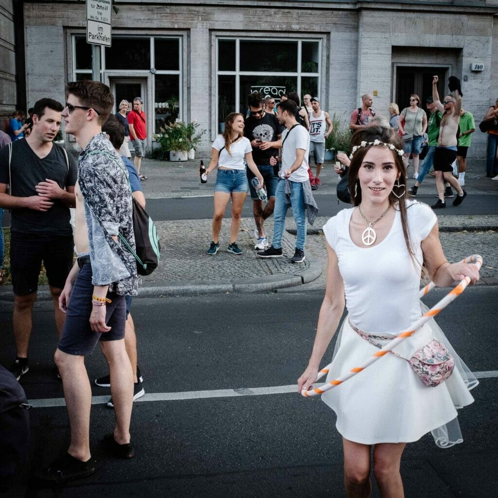 A woman wearing white hula hooping on a street with a crowd around.