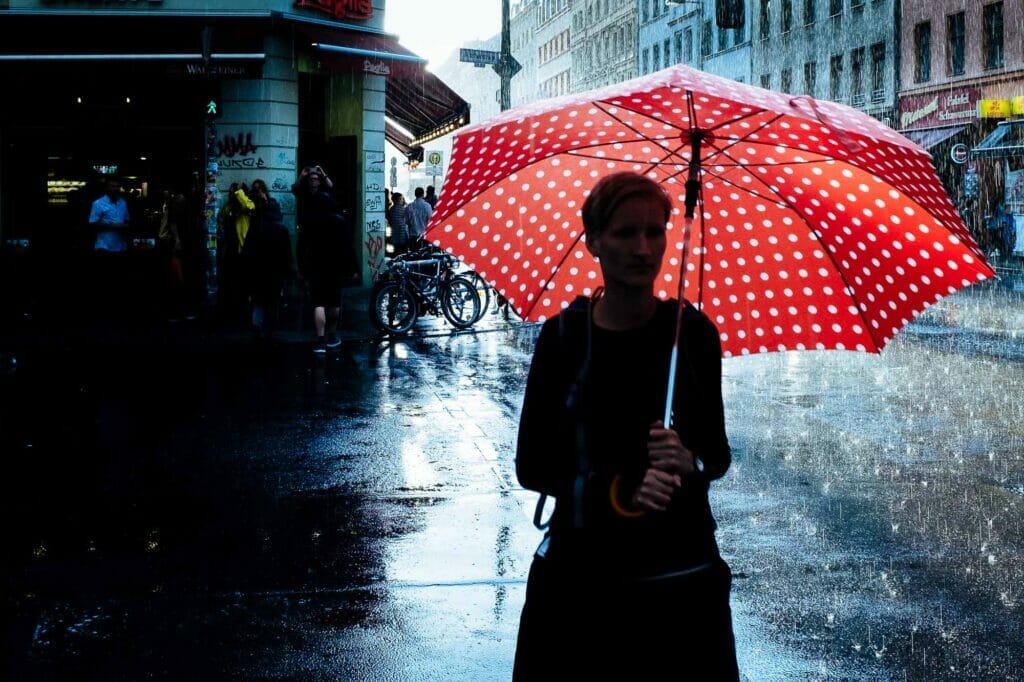 A woman with short blonde hair holding a red umbrella with white polka dots in rain.