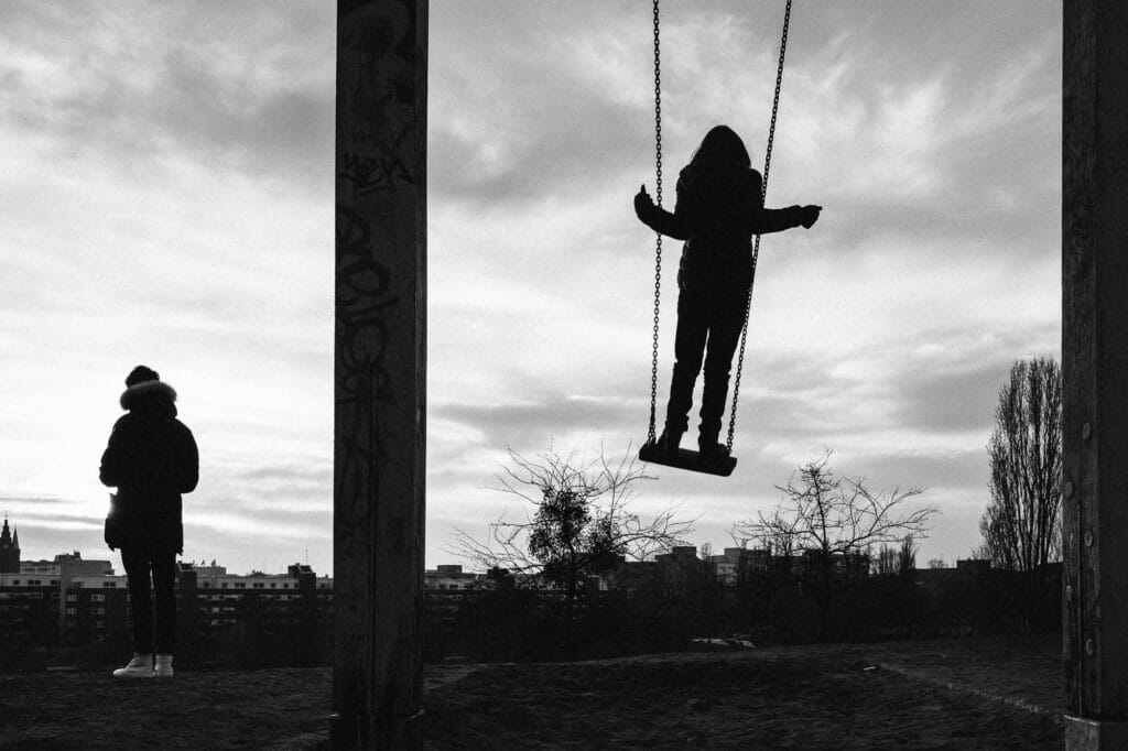 A silhouette of a kid standing on a swing and swinging.