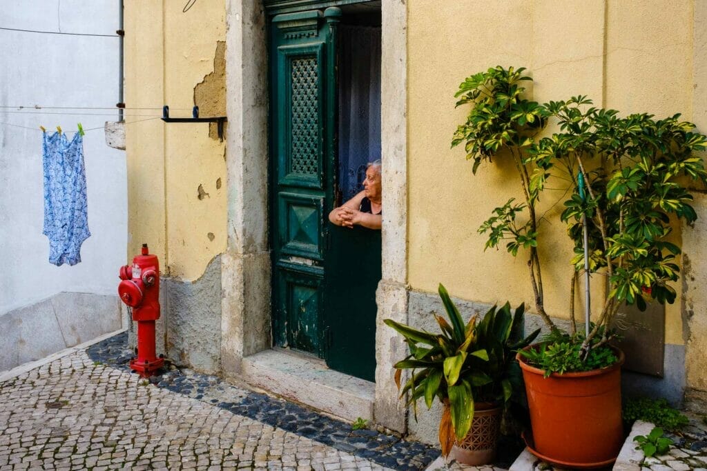 A woman looking out of her home. There are potted plants, a fire hydrant, and a clothesline