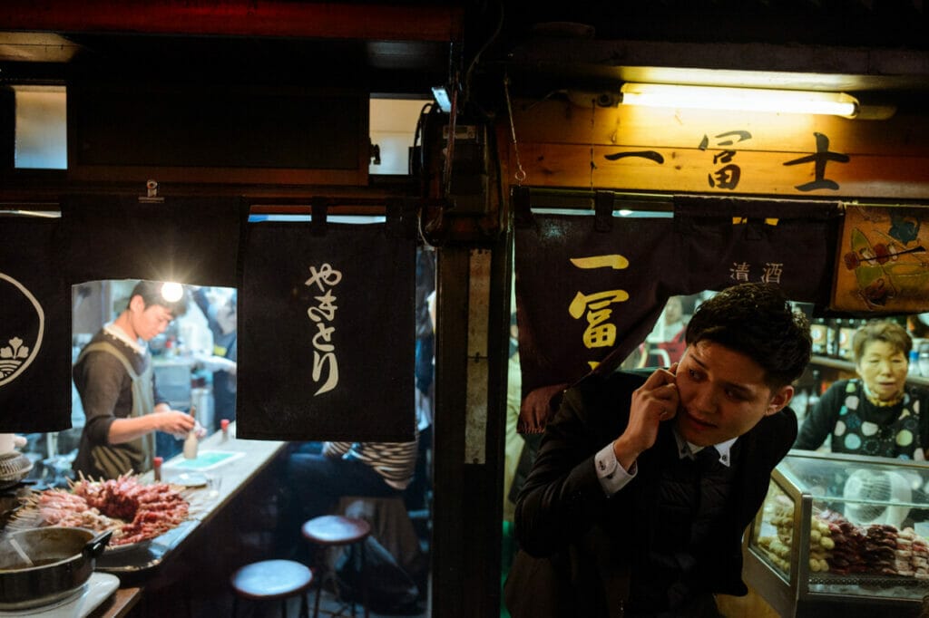 A man talking on a cell phone while looking out of a small restaurant in Japan.