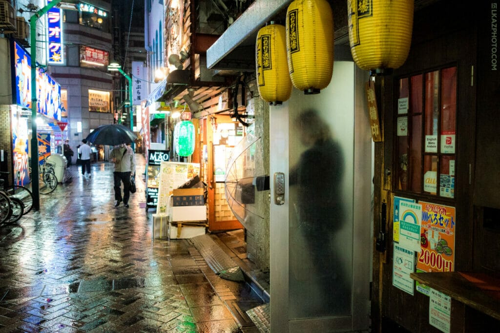 The outline of a person behind a frosted glass door on a alley in Japan while it's raining.